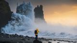 Explorador de pie en una costa rocosa con olas espectaculares y el atardecer como telón de fondo en Islandia.