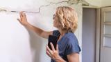 Una mujer revisa una pared de su casa en la que se puede apreciar una grieta de un tamaño considerable
