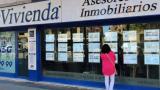 Mujer mirando anuncios de venta y alquiler en el escaparate de una inmobiliaria.