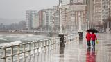 Una pareja anda por la calle bajo la lluvia en un día frío de invierno en Gijón (Asturias)