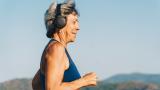 Mujer mayor con auriculares corriendo por el terraplén, día soleado de verano.