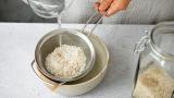 High angle view of woman hands washing white rice in colander in a bowl. Close-up of female cooking rice in kitchen.