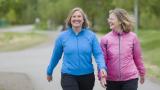 Dos mujeres mayores de sesenta y tantos años haciendo ejercicio caminando juntas por un sendero pavimentado.