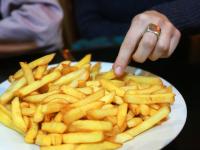 Manos de una persona comiendo de un plato de patatas fritas en un bistró parisino.