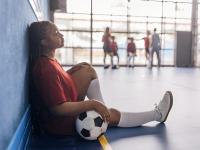 Una joven jugadora de fútbol sentada con la pelota contra la pared azul