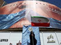 Una mujer sostiene una bandera iraní ant una valla antiestadounidense que muestra al presidente Donald Trump amordazado por el estrecho de Ormuz, en Teherán, el 25 de mayo de 2026.