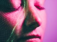 Plano cercano del rostro de una mujer con ojos cerrados en un fondo rosa mientras hay luces verdes iluminándose en su cara