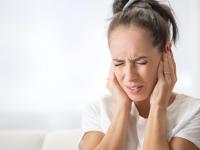 Una mujer tapándose los oídos con las manos debido al ruido o al dolor de oído, con el ceño fruncido.