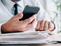 Una persona revisando el móvil junto a varios documentos de trabajo