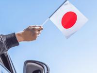 Una persona sacando una bandera de Japón por la ventanilla de un coche.