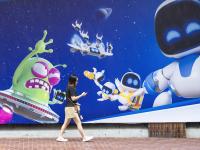 Una mujer pasea junto al mural de Astrobot, la mascota de PlayStation 5