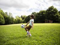 Un niño juega al fútbol en una zona verde.