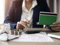 Una mujer haciendo cuentas con una calculadora sobre lo que tiene apuntado en la libreta de ahorros