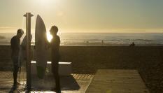 Dos surferos en la ducha de una playa al atardecer.