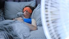Una mujer durmiendo con un ventilador.