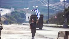 Un colono alza una bandera de Israel frente a palestinos en una carretera de Cisjordania