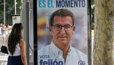 Una mujer junto a una marquesina de una para de autobús con propaganda electoral de Alberto Núñez Feijóo.