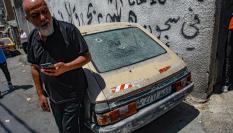 Un palestino, de pie, junto a su vehículo en el que se pueden ver marcas de bala en los cristales.