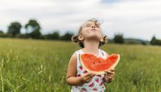 Una niña muerde una sandía y es feliz en una imagen de archivo.