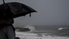 Una persona se cubre bajo un paraguas mientras ve una playa