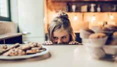 Imagen de archivo de una pequeña observando con interés un plato de galletas.