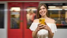 Imagen de archivo de una mujer leyendo algo en su móvil y riéndose, ante un vagón de Rodalies.