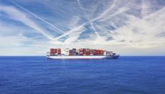 Un buque cargado de contenedores navega bajo un cielo lleno de nubes bajas.