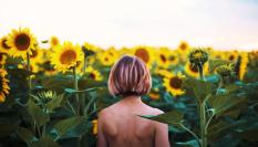 Imagen de una mujer caminando desnuda entre girasoles.
