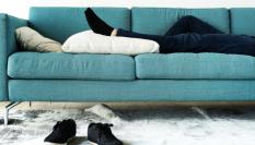 Las piernas de una persona sobre un sofá mientras que su calzado permanece en el suelo.