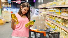 Imagen de archivo de una mujer eligiendo entre dos marcas de aceite de oliva en un supermercado.