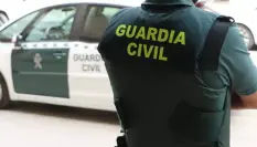 Un agente de la Guardia Civil, de espaldas, junto a un vehículo oficial.