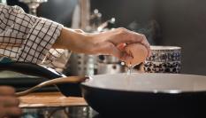 Una persona cascando un huevo en el borde de la sartén.