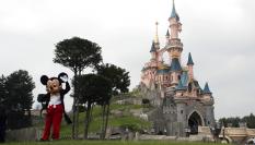 Mickey Mouse saluda con castillo de la Bella Durmiente, símbolo de Disneyland.