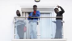 Algunos de los 240 migrantes de origen subsahariano llegados en los últimos días a Canarias saludan desde la terraza de una habitación del hotel Urban Beach de la localidad malagueña de Torrox, donde se alojarán tras ser trasladados por el Gobierno, con la colaboración de la Cruz Roja.