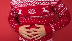 Un hombre en jersey navideño arrepintiéndose de comer demasiado.