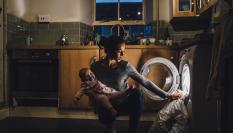 Imagen de archivo de una madre poniendo la lavadora mientras sostiene a su bebé.