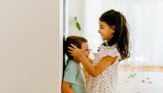 Una niña mide la altura de su hermano y lo marca en la pared de su casa.