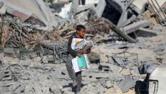 Un menor palestino recoge material escolar entre los escombros de la escuela Al-Urube, atacada por Israel en el campamento de Nuseirat.