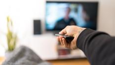 Un hombre tumbado en el sofá cambia de canal de televisión.