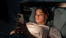 Imagen de archivo de una mujer joven en la cama con un móvil.