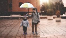 Imagen de archivo de un niño cubriendo a otro con un paraguas.