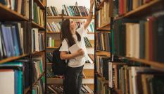 Una mujer cogiendo un libro en la biblioteca.