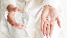 Una persona con unas pastillas y un vaso de agua.