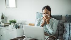 Una mujer con gripe, en cama con el ordenador del trabajo.