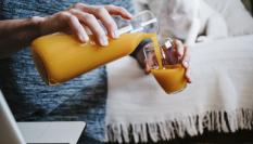 Un hombre echando zumo de naranja en un vaso.