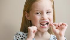 Una niña pasándose el hilo dental.