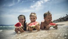 Unos niños comiendo sandía en la playa.