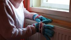 Una persona con guantes se agarra a un radiador para no pasar frío en casa.