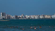 Turistas y vecinos disfrutan en la playa de El Postiguet de un día soleado y calor.