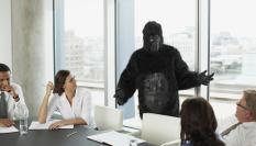 Ilustración de una persona siendo vista como un gorila, durante una reunión empresarial.